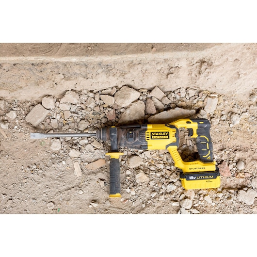 Stanley FMCD900M2S brushless rotary hammer drill with 18V lithium battery on rocky ground, top view.