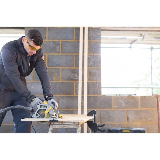 Photo of STANLEY FME301 circular saw in use cutting wood on worksite, operator wearing gloves and safety gear.