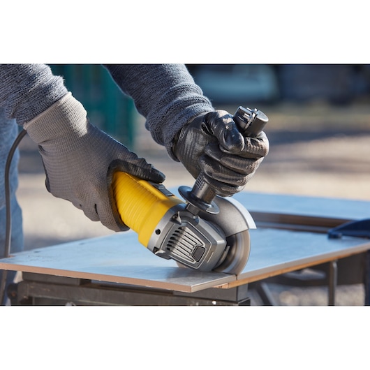 STANLEY FMEG220KA angle grinder cutting a tile, close-up view with gloved hands operating tool.