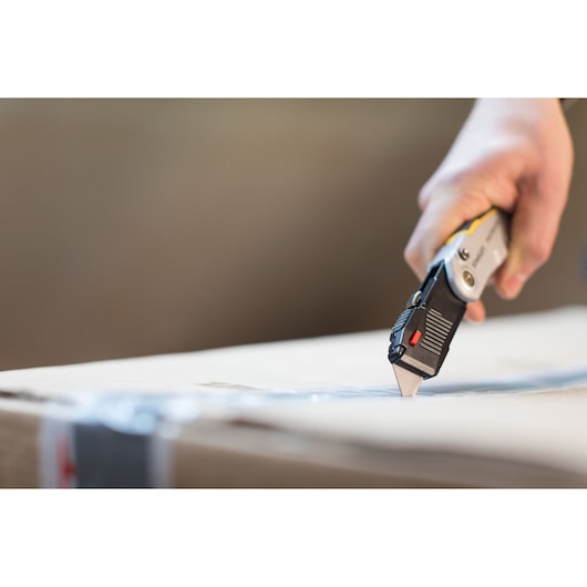 Photo of STANLEY FMHT0-10320 utility knife cutting cardboard box, close-up angle.