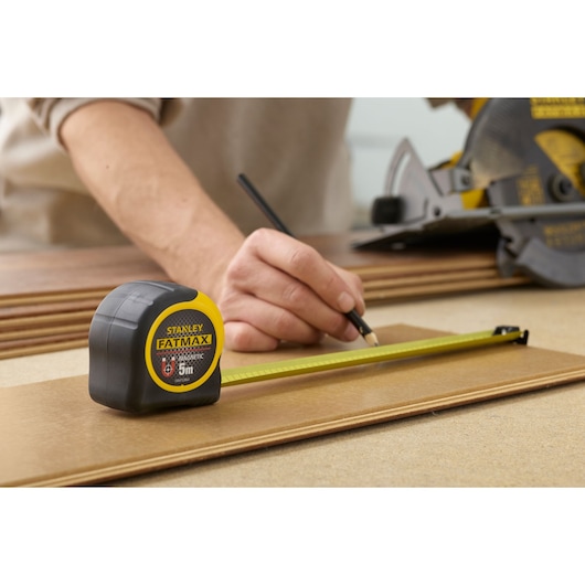 STANLEY FMHT0-33864 tape measure used for marking wood, yellow and black casing, close-up photography.