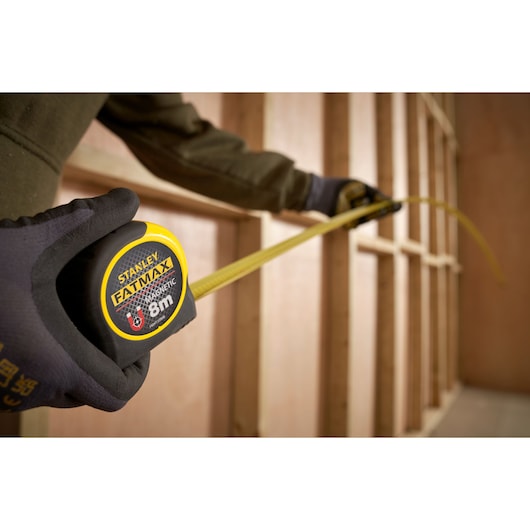 Stanley FMHT0-33868 tape measure with yellow blade extended in a construction framing setting.