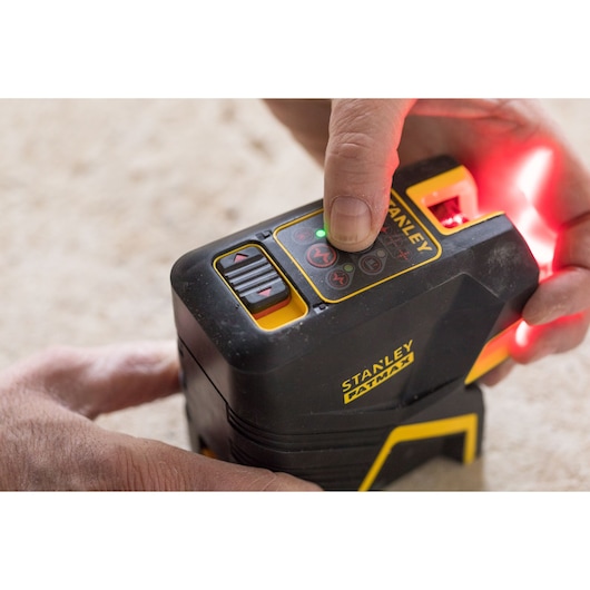 Photo of STANLEY FMHT1-77415 laser level being operated by hand on beige surface.