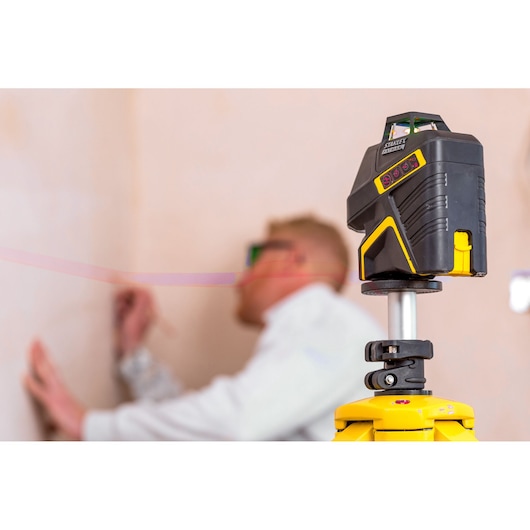 STANLEY FMHT1-77416 laser level on tripod in use by worker marking wall.