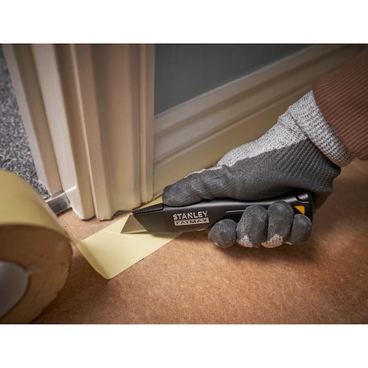 STANLEY FMHT10500-0 utility knife cutting masking tape near door frame, gloved hand holding knife.