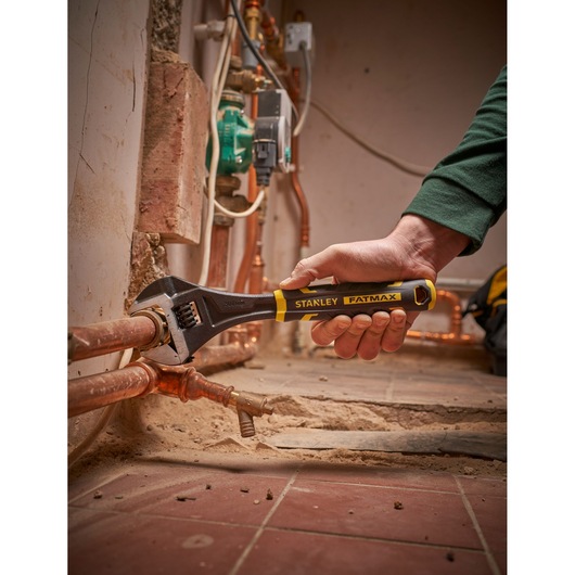 Photo of STANLEY FMHT13125-0 adjustable wrench being used on copper pipes in a plumbing setting.