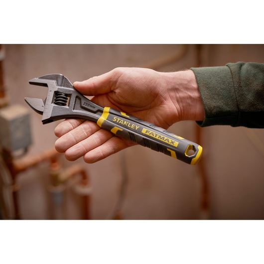 Photo of STANLEY FMHT13125-0 adjustable wrench with black and yellow handle, held in hand, plumbing background.