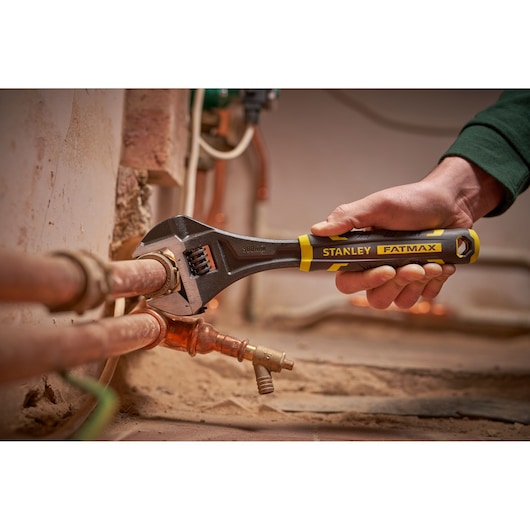 STANLEY FMHT13126-0 adjustable wrench being used on copper pipes, close-up view of tool in action.