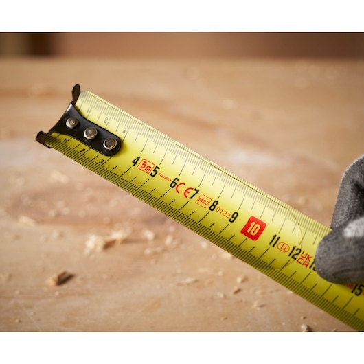 STANLEY FMHT31725-0 tape measure with yellow blade, close-up on measurement markings in workshop.