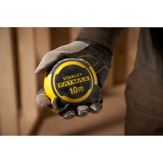 STANLEY FMHT33005 10m FATMAX tape measure held in a gloved hand, close-up indoor setting.