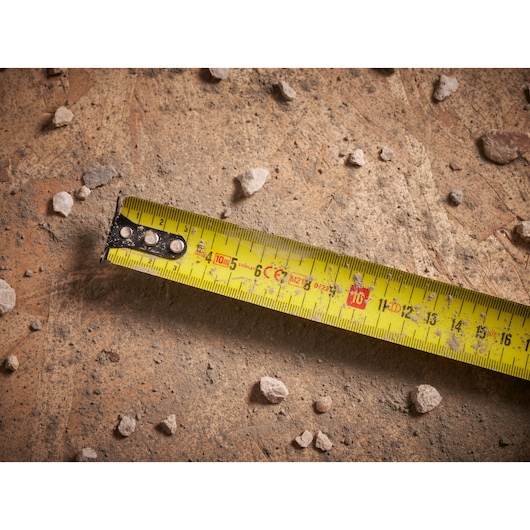 STANLEY FMHT33005 tape measure photography showing yellow blade on dusty, rocky surface.