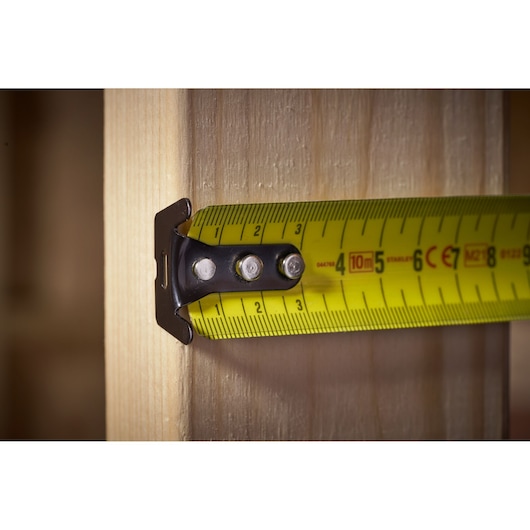 STANLEY FMHT33005 tape measure close-up, yellow blade extended against wooden surface.