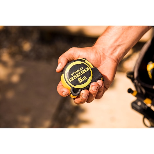 Photo of STANLEY FMHT33100-0 FATMAX 5m tape measure held in a hand, yellow and black compact design.