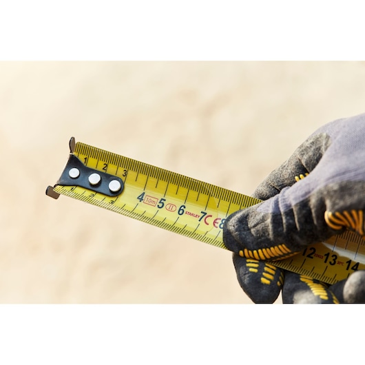 STANLEY FMHT36142-0 tape measure in use, yellow blade with clear markings, held by gloved hand, close-up.