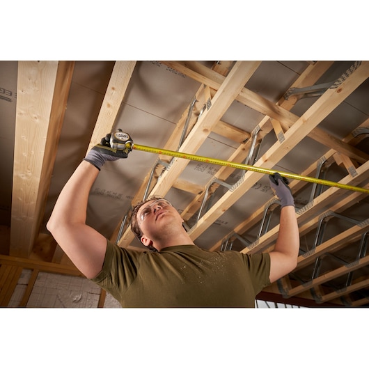 STANLEY FMHT38214-0 tape measure used to measure wooden ceiling beams in a construction interior.