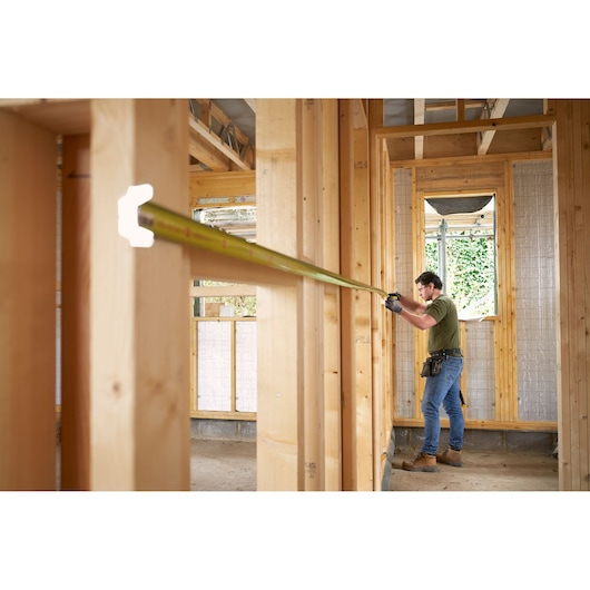 STANLEY FMHT38232-0 tape measure extended by worker inside wooden house frame, side view, construction site.