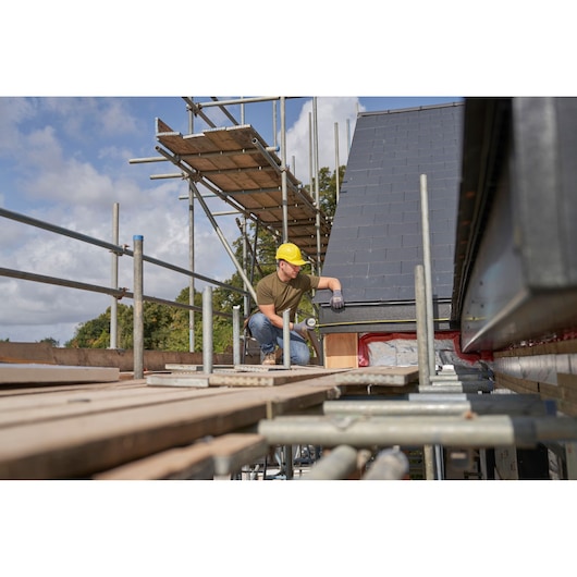 STANLEY FMHT38232-0 tape measure used by worker on roof scaffolding, construction site outdoors.