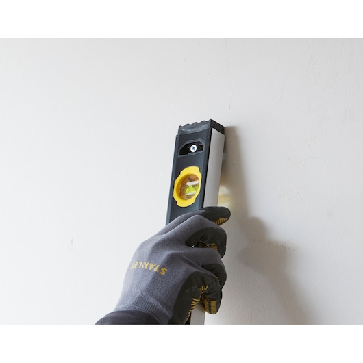 Photo of STANLEY FMHT42447-1 spirit level held by gloved hand against a wall, product in use.