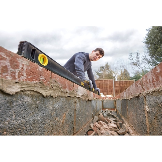 STANLEY FMHT42561-1 spirit level in use on brick wall construction, outdoor angle.