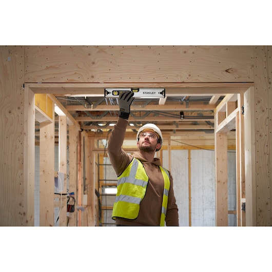 Photo of a worker using a STANLEY FMHT43671-1 spirit level on a wooden door frame at a construction site.