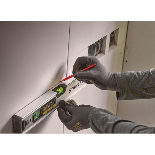 Photo of STANLEY FMHT43671-1 spirit level held against wall, gloved hands marking with pencil.