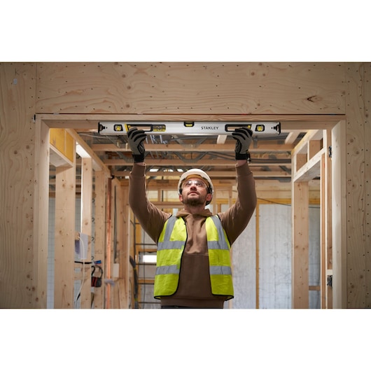 Photo of STANLEY FMHT43675-1 spirit level in use on a wooden door frame during construction.