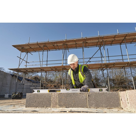 Photo of worker using STANLEY FMHT43676-1 spirit level on construction site with scaffold in background.