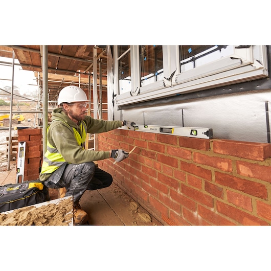Photo of STANLEY FMHT43677 spirit level in use by a builder on a brick wall at a construction site.