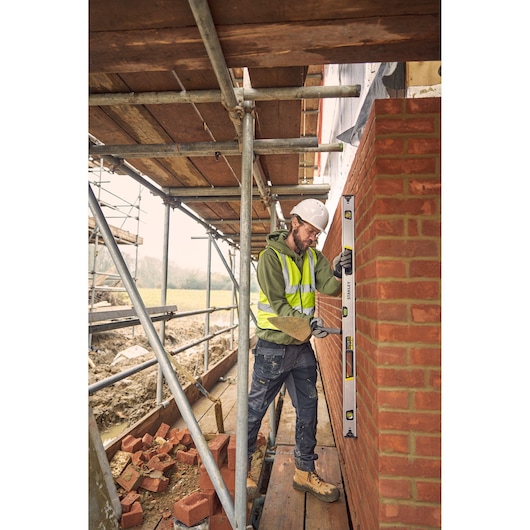 STANLEY FMHT43677 spirit level used by construction worker to check brick wall alignment on building site.