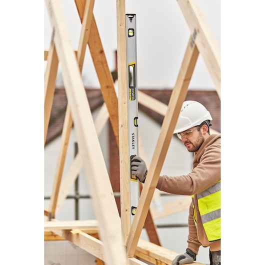 STANLEY FMHT43677 spirit level used vertically by a worker on wooden beams at a construction site.