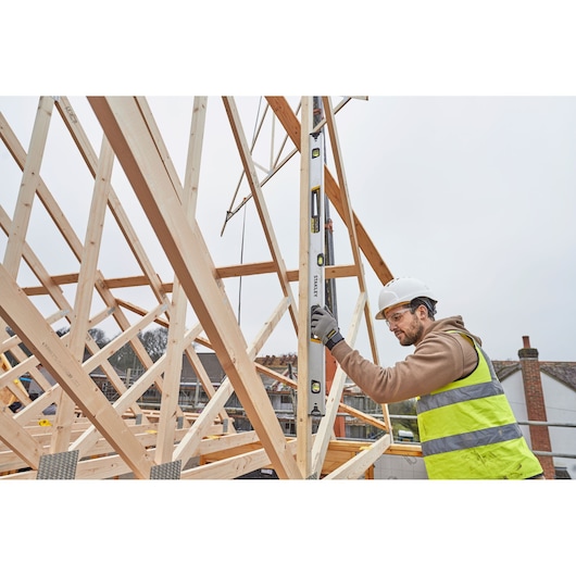 STANLEY FMHT43677 spirit level used vertically by worker on wooden building frame at construction site.