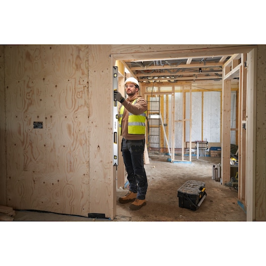 STANLEY FMHT43677 spirit level used by worker in high-visibility vest on construction site with wooden frame walls.