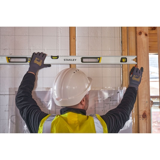 STANLEY FMHT43677 spirit level held by construction worker wearing helmet and safety vest against wall.