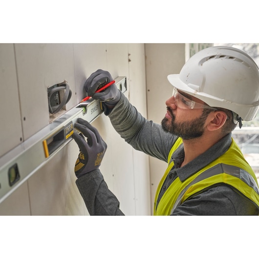 STANLEY FMHT43677 level used by worker in safety gear marking wall, close-up photography.