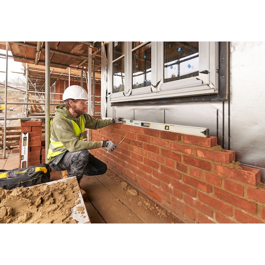 STANLEY FMHT43678-1 spirit level used by a worker checking horizontal alignment on a brick wall, side view.