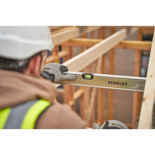 STANLEY FMHT43679-1 spirit level held by worker with gloves, used for leveling wooden frame at construction site.