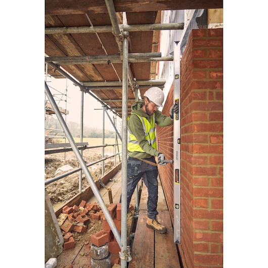 STANLEY FMHT43680-1 spirit level used by a construction worker checking a brick wall's alignment on scaffolding.
