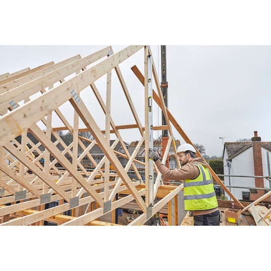 STANLEY FMHT43680-1 spirit level used by worker measuring wooden roof frames at construction site.