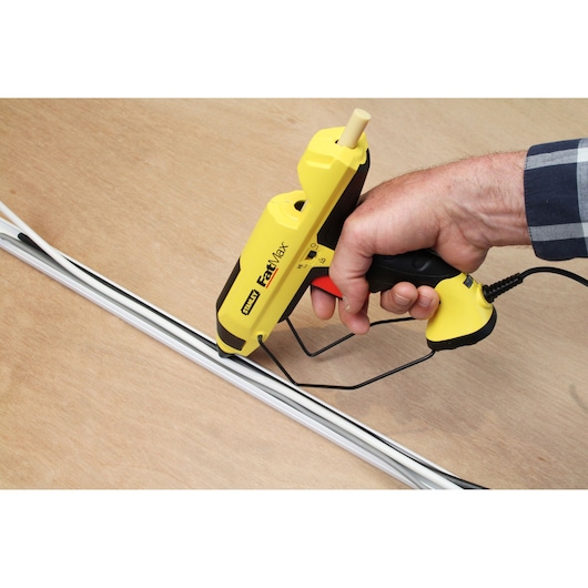 STANLEY FMHT6-70418 yellow glue gun in use applying adhesive to white trim on wood surface.