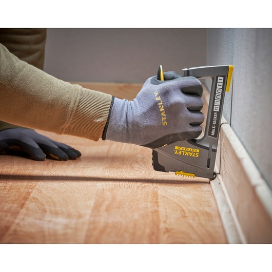 Photo of a hand wearing Stanley gloves using a STANLEY FMHT6-70868 multi-tacker on floor trim, side angle.