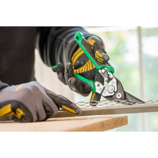 STANLEY FMHT73557-0 aviation snips with green handles cutting metal mesh, close-up in use.