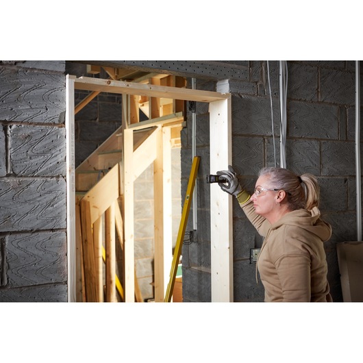 STANLEY FMHT77165-0 laser distance measurer used on wooden door frame at construction site.