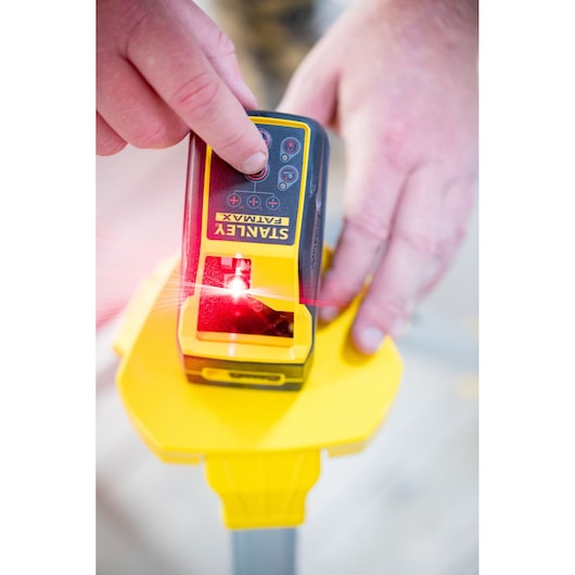 Photo of STANLEY FMHT77585-1 laser level device in use, emitting red laser, on yellow tripod base.
