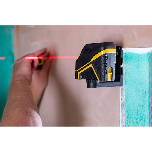 STANLEY FMHT77585-1 laser level projecting red line onto wall, used by hand for marking, side angle.