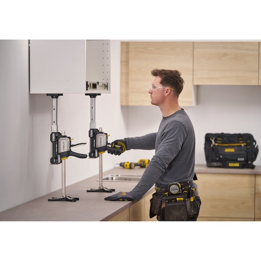 STANLEY FMHT83554-1 cabinet clamp holding wall cabinet during installation, with worker adjusting clamp in kitchen setting.