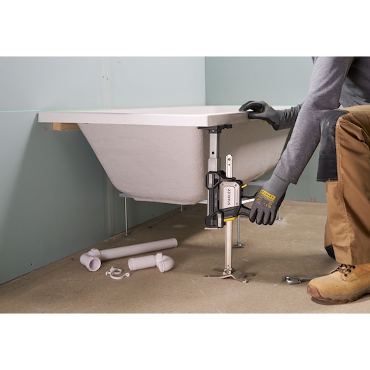 Photo of a STANLEY FMHT83554-1 support clamp in use adjusting a bathtub height during installation.