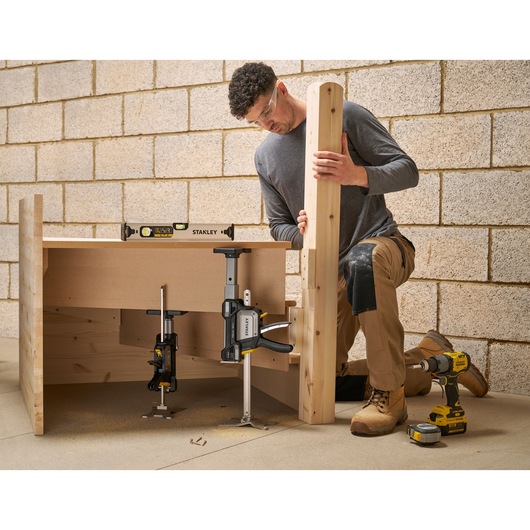 STANLEY FMHT83554-1 clamp holding wood in woodworking setup, side angle, with tools and person working.