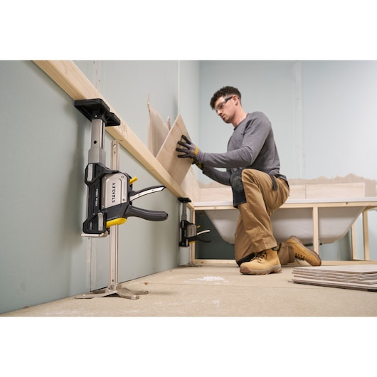 STANLEY FMHT83554-1 clamp securing wood to a wall during construction, person installing tiles in bathroom.
