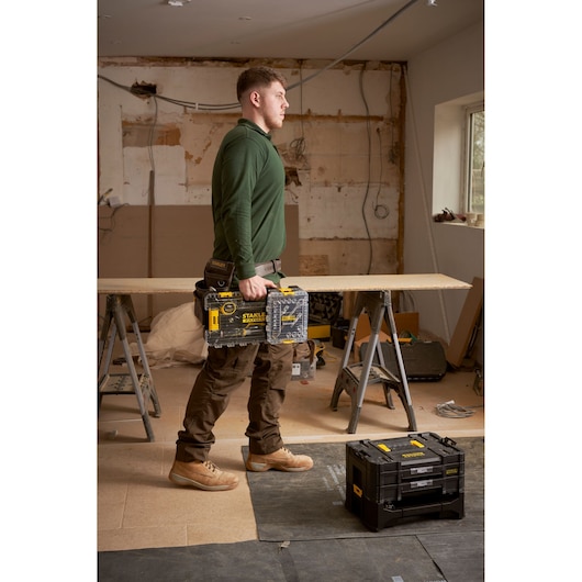 Photo of STANLEY FMMT98102-0 toolbox held by worker in workshop, with another STANLEY toolbox on the floor.