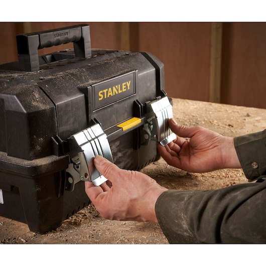 STANLEY FMST1-71219 black toolbox with metal latches on workbench, hands opening front locks